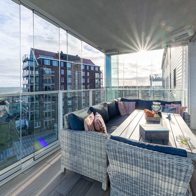 Modern balkon met glazen schuifwanden, stijlvol ingericht met een loungeset en uitzicht op de stad en zee.